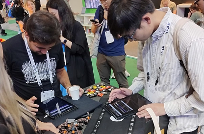 Visitantes interagindo com tablets em uma mesa do estande "42" na ICLR, durante a operação onsite com atendimento e suporte da equipe.